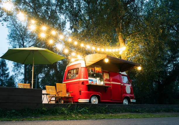 Empty small Street Food Track with an illumination standing in the deserted night park. Near food trailer are folding tables and chairs