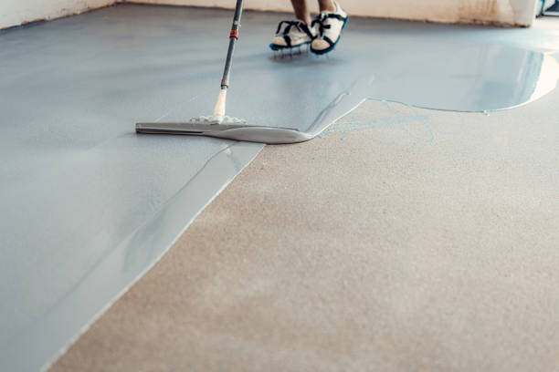 A construction worker applying grey epoxy resin in an industrial hall