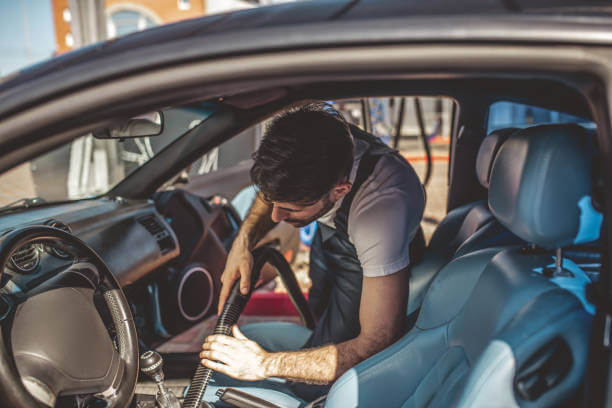 Professional service station worker in the uniform cleaning the vehicle upholstery with a vacuum cleaner