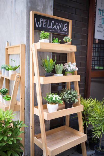 many pots of decoration plants put on the wooden shelfs in tree shop on sidewalk street