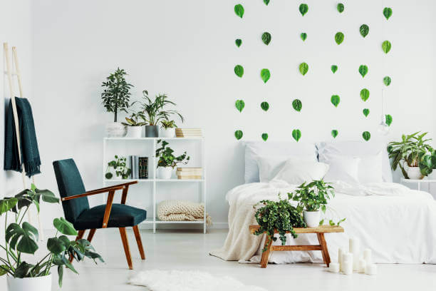 Green retro armchair in white bedroom interior with urban jungle and bed with white sheets