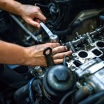 Car mechanic man at the garage fixing the engine. Hands of car mechanic with wrench in garage. Close up hands of unrecognizable mechanic doing car service and maintenance. Auto Service Business Concept. Pro Car Mechanic Taking Care of Vehicle. Checking Under the Car Hood.