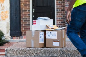 An unrecognizable mail man approaches the stack of boxes and envelopes left on the front porch of the home for pick-up.