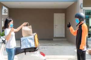 Asian woman pick up delivery food bag from box and thumb up form contactless or contact free from delivery rider with bicycle in front house for social distancing for infection risk.