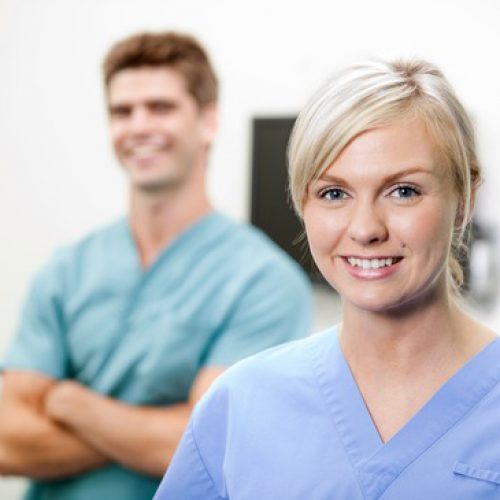 Portrait of young female vet in scrubs smiling with colleague standing in background