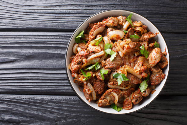 Armenian Tjvjik fried chicken offal liver, heart and stomachs with onions, tomatoes and spices close-up in a bowl on the table. horizontal top view from above