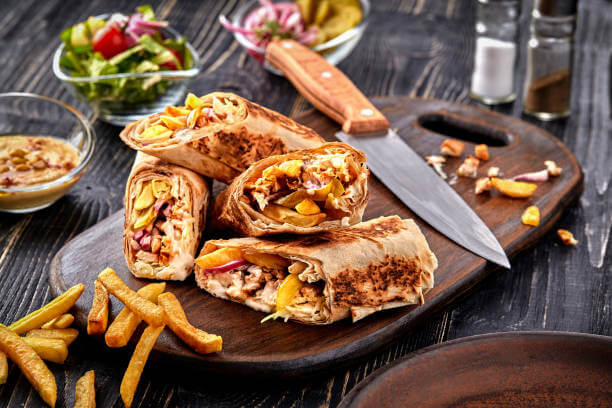 Middle Eastern Chicken Shawarma, Pita Sandwich, roll in a pita with fresh vegetables, cream sauce and french fries on wooden background. Selective focus. Lunch snack. Still life