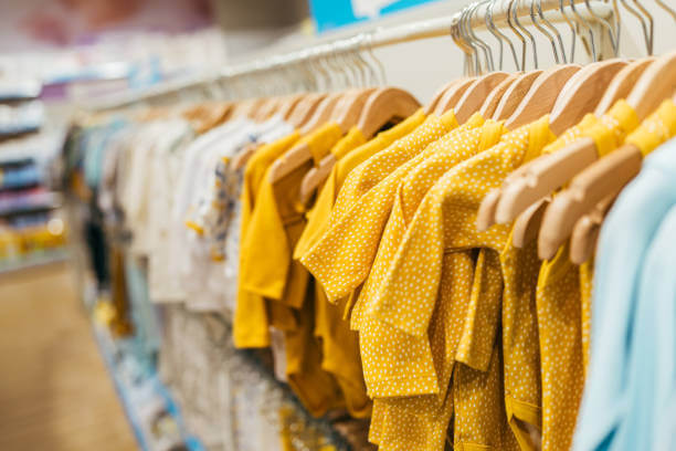 Beautiful baby clothes hanging arranged on rack in a modern store or shop. Shopping interior concept. No people.