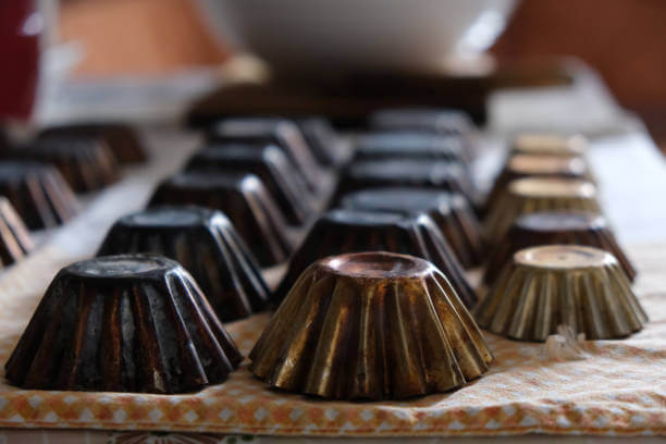 A stack of small rusty metal cupcake molds at kitchen table waiting to be filled with dough.