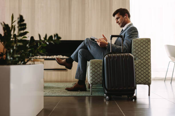 Businessman reading a magazine while waiting for his flight at airline terminal lounge. Entrepreneur at airport waiting area reading a magazine.