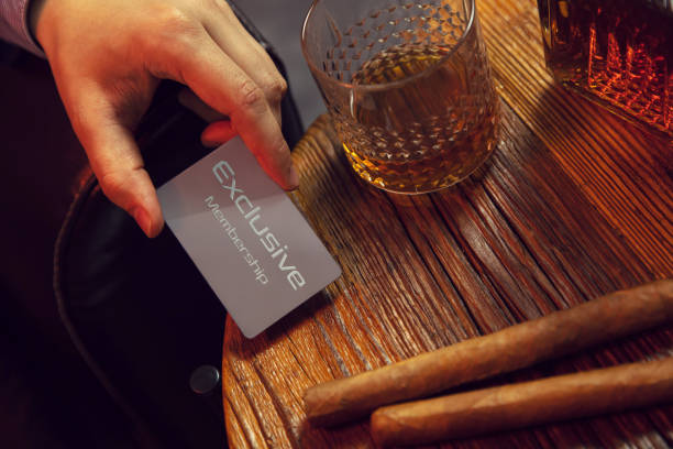 Man's hand puts exclusive membership card on the table. Gentleman's hand puts exclusive membership card on the wooden table with whisky in carafe and glass with cigars.