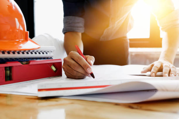 Young engineers using pen point to the blueprint paper to examine the structure of the building before presenting it at the conference. Architecture design concept.