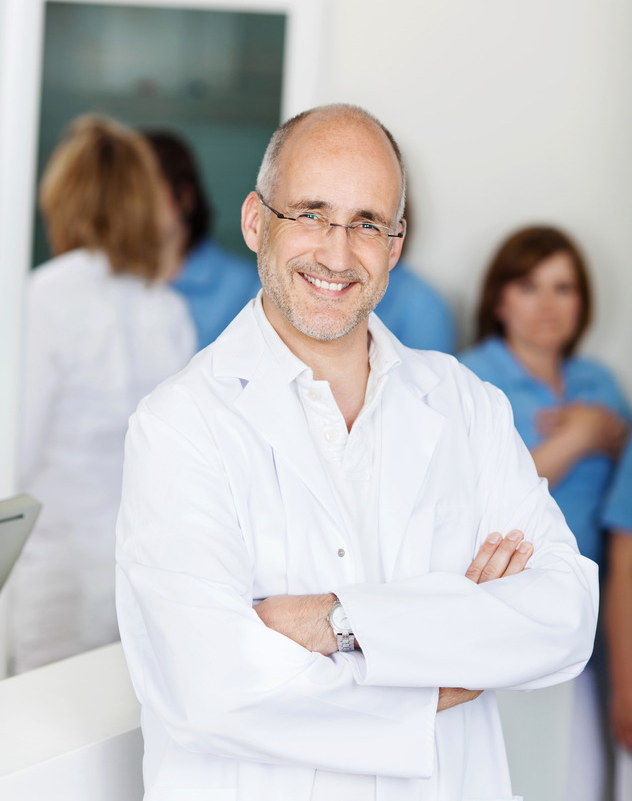 Portrait of male mid adult dentist smiling with assistants in background at clinic