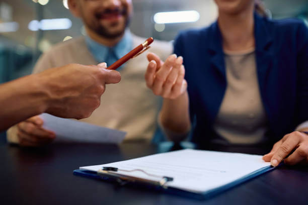 Close up of woman signing an agreement while being on a meeting with insurance agent with her husband.