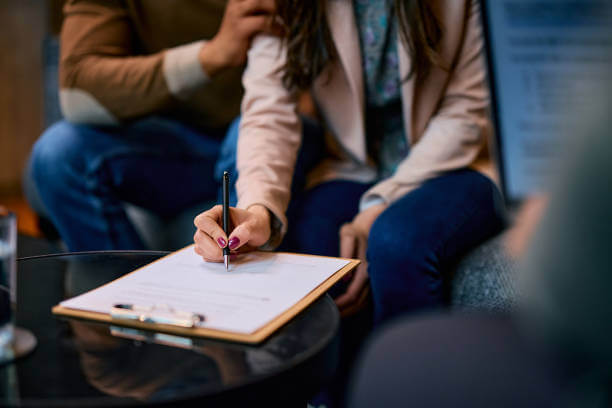 Close up of African American woman and her husband signing paperwork during a meeting with insurance agent.