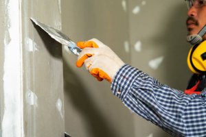 Construction worker using a putty knife with trowel plastering a wall in new house,Builders in hardhats with plastering tools indoors.