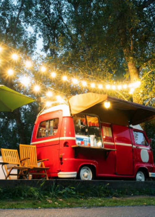 Empty small Street Food Track with an illumination standing in the deserted night park. Near food trailer are folding tables and chairs