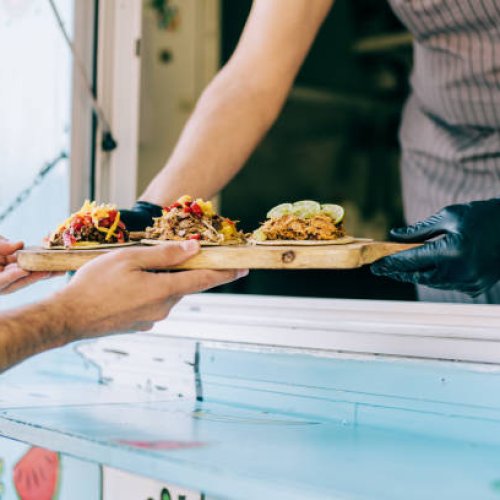 Cropped shot of young chef serving tasty tacos to male customer from the window of his food van.