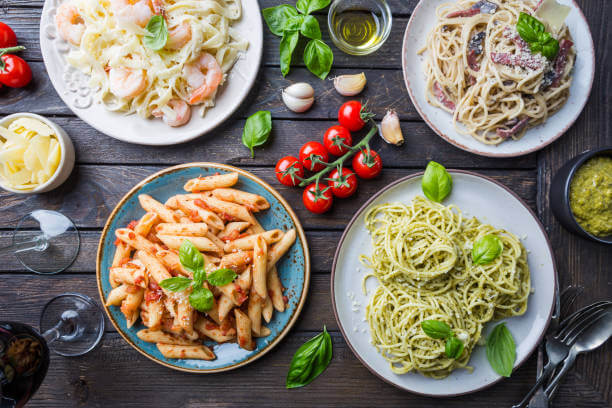 Several plates of pasta with different kinds of sauce over wooden background, top view. Concepts of Italian food.