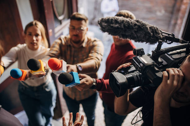 Group of people, female politician confronted by journalists with microphones.