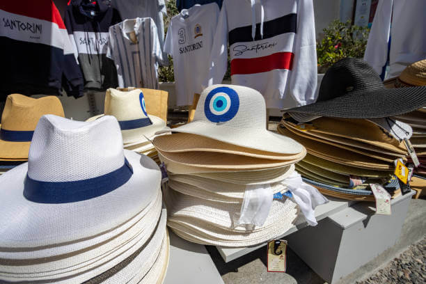 Evil Eye on Souvenir Hats at Gift Shop in Firá on Santorini in South Aegean Islands, Greece, with trademarked fonts in the background.