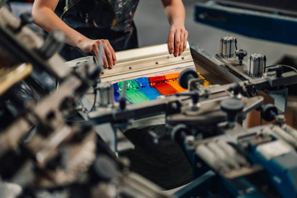 Close up of female experienced graphic technician's hands silkscreen printing with squeegee at printing workshop.Cropped picture of unrecognizable print shop worker suing rubber blade for screen print