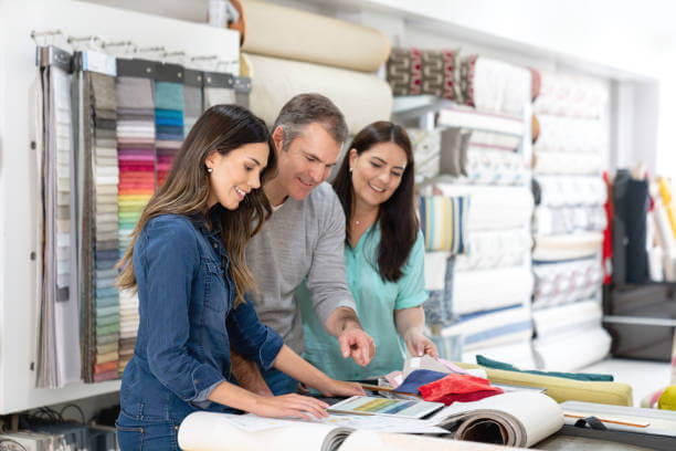 Happy interior designer with a couple choosing fabrics for a house project at a textile shop - business concepts