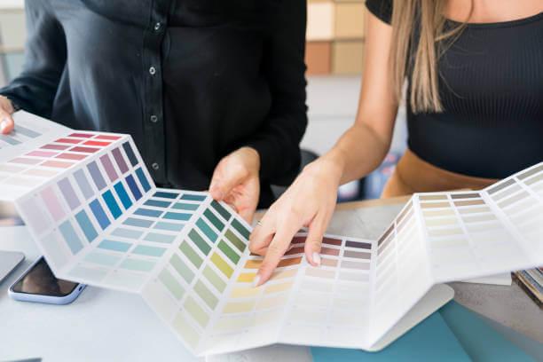 Close-up of two women choosing samples of wall paint. Interior designer consulting a client looking at a color swatch. House renovation concept