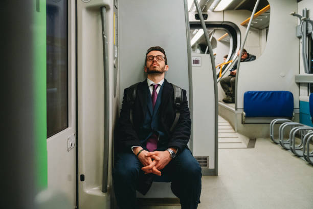 A tired businessman is going to work with a train. He's wearing a suit and a coat.