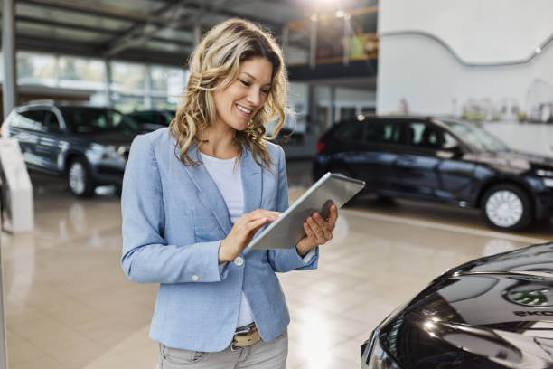 Happy female salesperson working on touchpad in a car showroom.