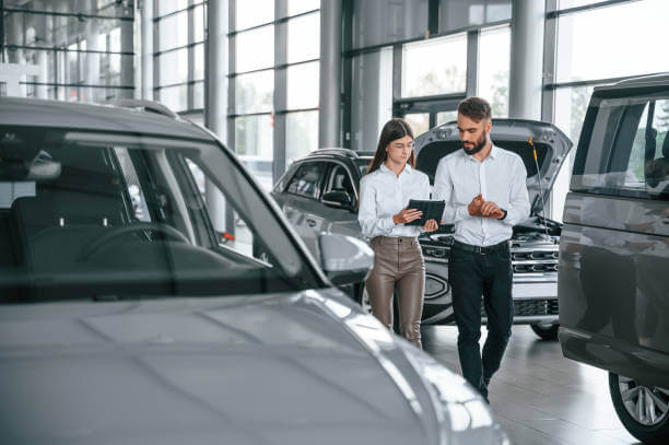 Walking forward and talking. Man with woman in white clothes are in the car dealership together.